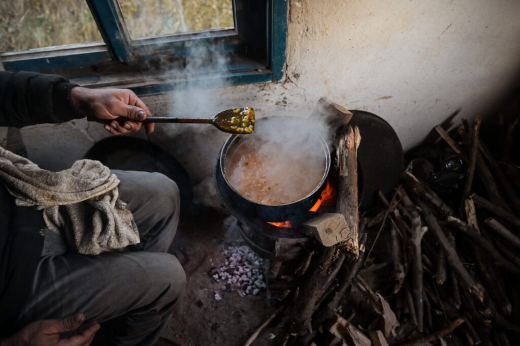 Ein Schutzsuchender kocht Essen über einem Feuer, nur die Hände sind zu sehen